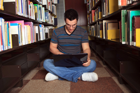 Image of a student sitting on library floor between stacks
